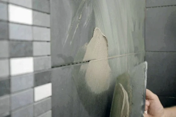 Person verfugt dunkle Wandfliesen.